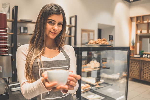 El trabajador del café sosteniendo una taza de café cerca de la vitrina.