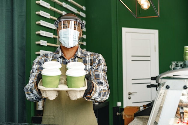 Trabajador de la cafetería con máscara médica mientras está de pie en el mostrador de la cafetería