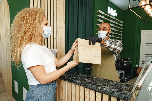 Trabajador de cafetería masculina dando orden al cliente con mascarilla facial