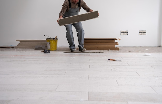 Trabajador calificado instalando baldosas cerámicas con efecto madera en el piso Trabajador haciendo pisos laminados en el sitio de construcción del nuevo apartamento