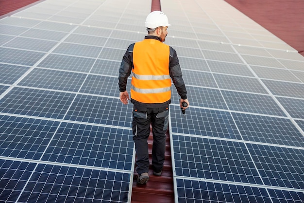 Un trabajador caminando por el techo entre paneles solares y preparándose para arreglarlo