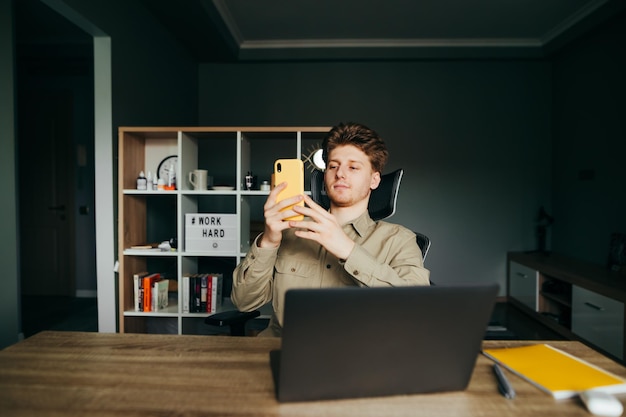 Foto trabajador en una camisa trabaja en casa en un trabajo remoto se sienta en el trabajo con una computadora portátil y usa un teléfono inteligente