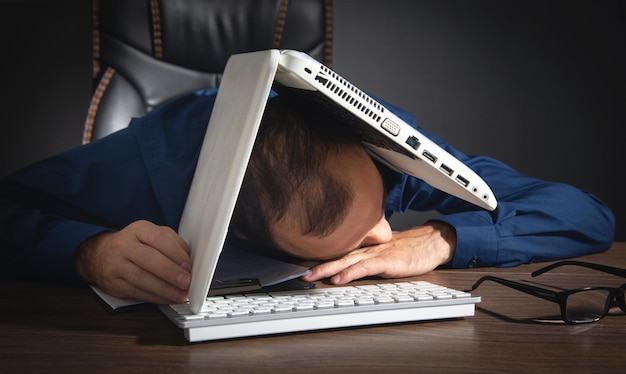 Trabajador cansado durmiendo en el escritorio con una laptop