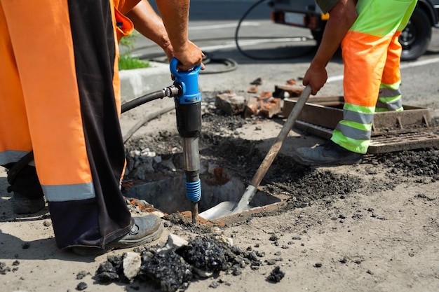 Un trabajador de la carretera está desmantelando el asfalto de la calle y el drenaje antiguo con un martillo neumático