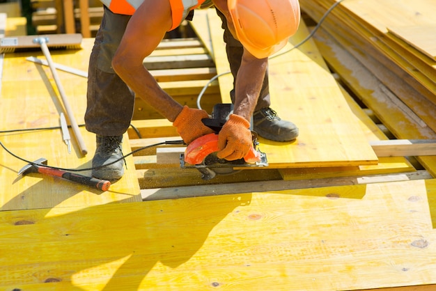 Trabajador en casco de seguridad aserrar una tabla de madera de cerca