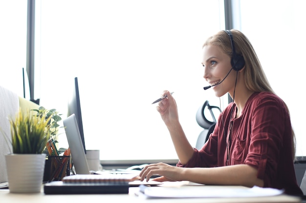 Trabajador de centro de llamadas hermoso en auriculares está trabajando en la oficina moderna.