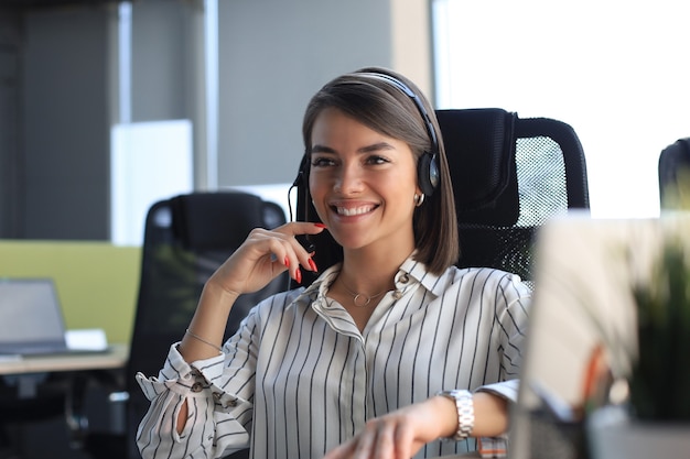 Trabajador de centro de llamadas sonriente hermosa en auriculares está trabajando en la oficina moderna.
