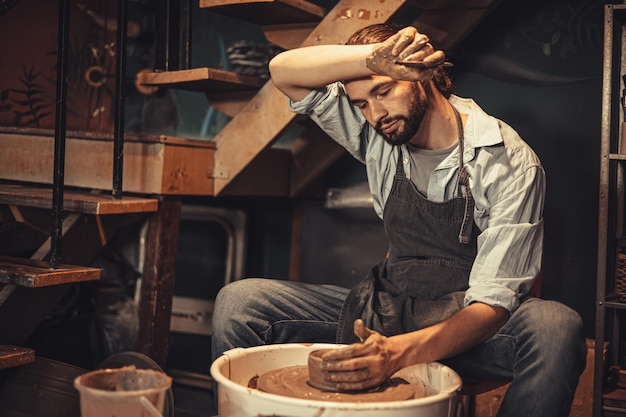 Trabajador de cerámica hecho a mano macho cray pot con cansancio agotado por el trabajo duro durante la noche intente