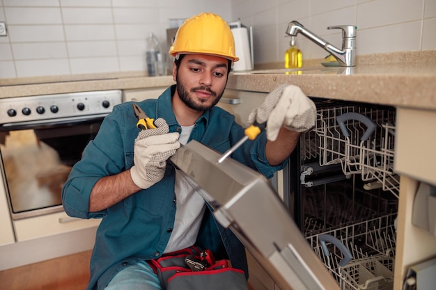 Trabajador concentrado con ropa especial reparando lavaplatos en una cocina moderna