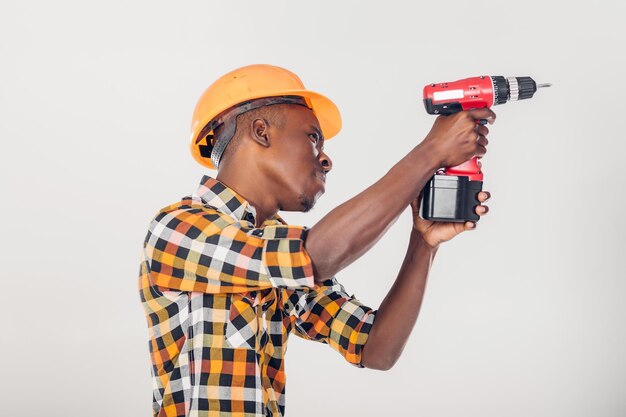 Trabajador de la construcción afroamericano en casco utiliza destornillador eléctrico