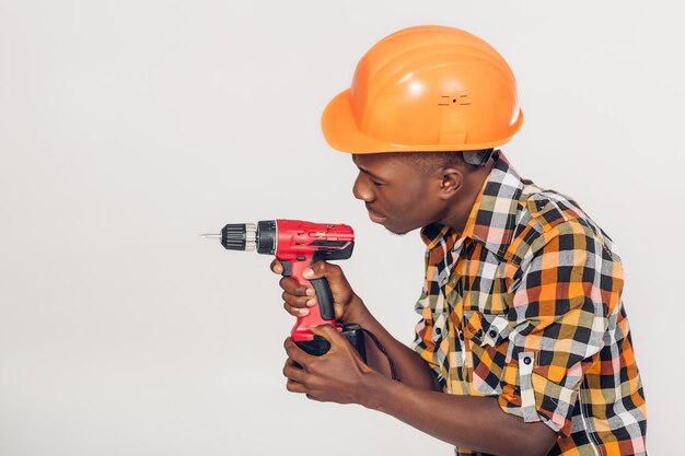 Trabajador de la construcción afroamericano en casco utiliza destornillador eléctrico