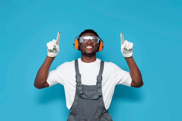 Trabajador de construcción afroamericano en uniforme apuntando hacia arriba sobre un fondo azul