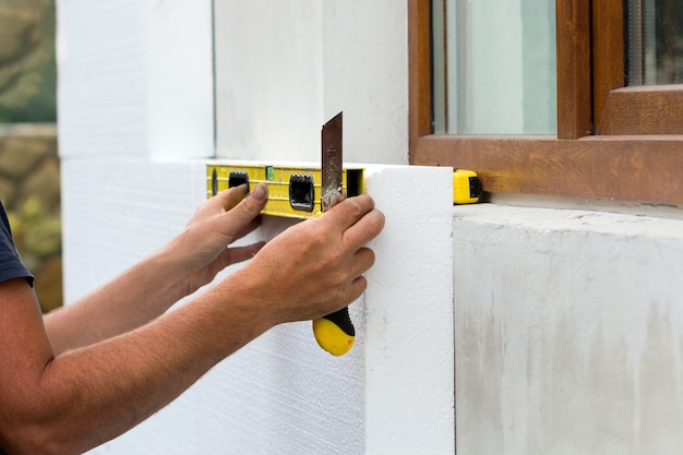 Trabajador de la construcción aislante de la pared de la casa con lámina de espuma de poliestireno.