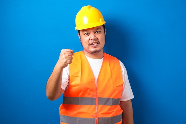 Trabajador de la construcción asiática hombre vestido con chaleco naranja y casco de seguridad con puño cerrado