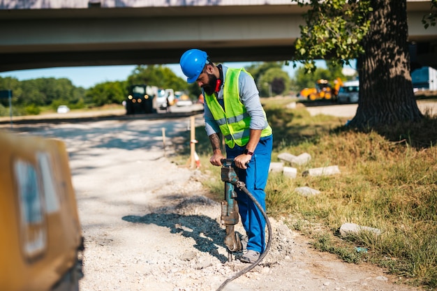 Trabajador de la construcción de carreteras de sexo masculino joven en su trabajo. Día soleado. Luz fuerte.