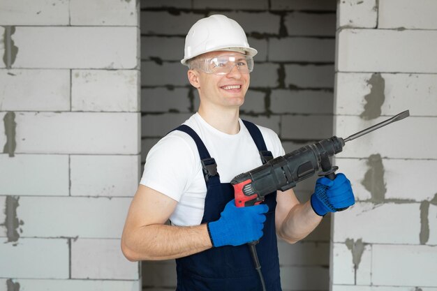 Trabajador de la construcción en un casco blanco sostiene un taladro eléctrico. Herramientas profesionales.