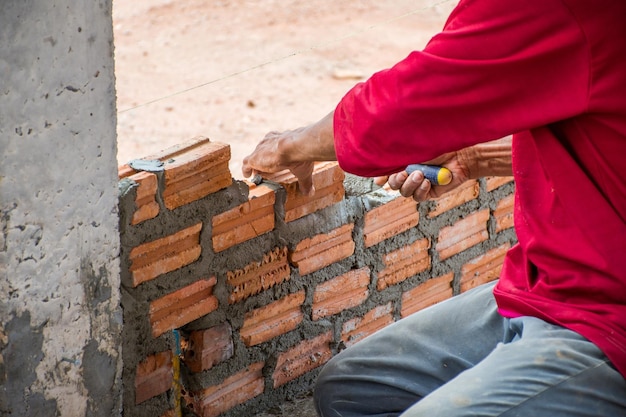 Foto trabajador de la construcción colocando ladrillos sobre cemento para construir paredes exteriores.