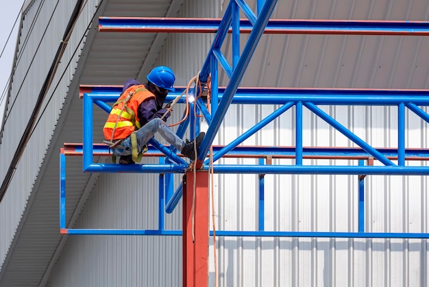 Trabajador de la construcción con equipo de seguridad soldando metal en la estructura del techo del edificio del almacén