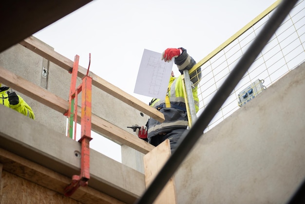 Un trabajador de la construcción está de pie en un andamio con un walkie-talkie y una hoja de dibujo de diseño