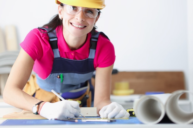 Trabajador de la construcción femenina sonriente en casco amarillo inclinado sobre planos