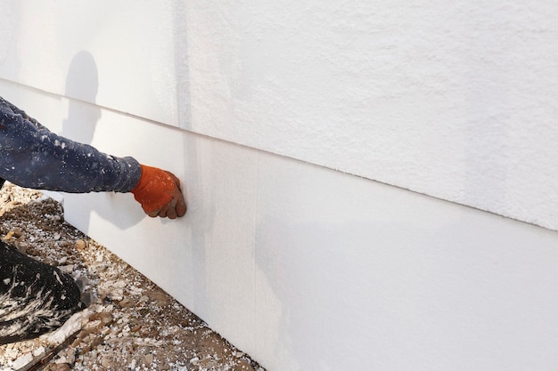 Trabajador de la construcción instalando láminas de aislamiento de espuma de poliestireno en la pared de la fachada de la casa para protección térmica