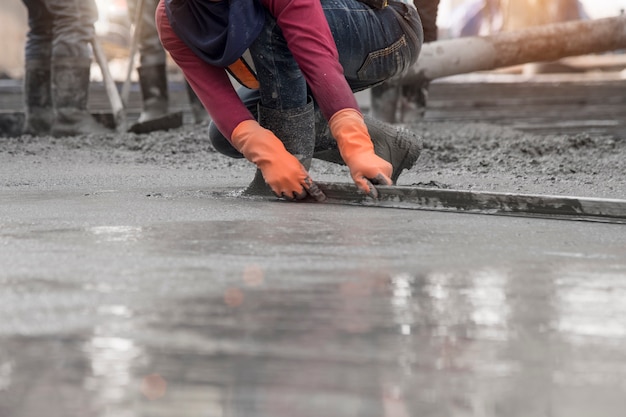 Trabajador de la construcción con llana de hormigón mojado en la parte superior de la losa de piso nuevo constructio