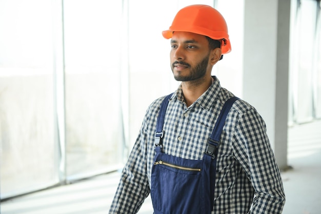 Trabajador de la construcción masculino indio de pie en uniforme y sombrero duro en el sitio de construcción