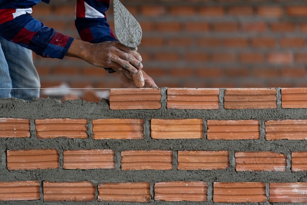 Trabajador de construcción profesional de la mano del primer que pone ladrillos en nuevo sitio industrial