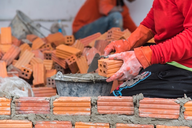 Foto trabajador de la construcción que pone ladrillos y que construye la pared en sitio de la casa.