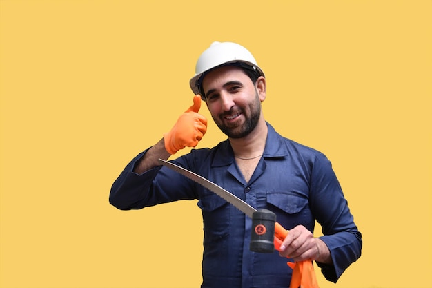 Trabajador de la construcción que se siente feliz sosteniendo un serrucho y mostrando ok thumbs up modelo paquistaní indio