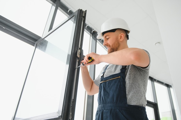 Foto trabajador de la construcción reparando una ventana de plástico con un destornillador en el interior, espacio para texto. diseño de pancartas