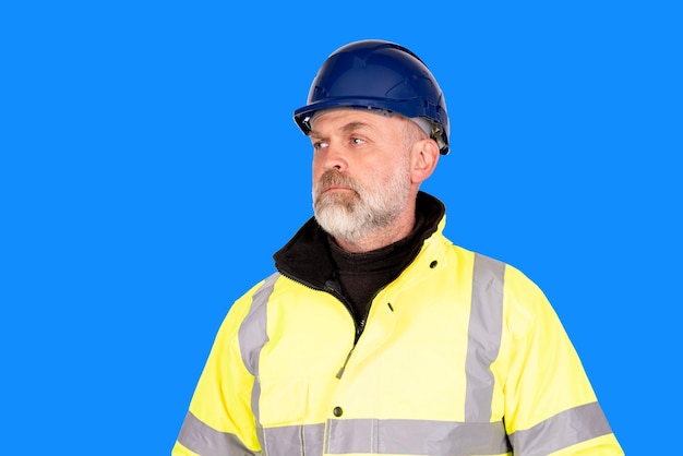 Un trabajador de la construcción con un sombrero azul y un abrigo hiviz amarillo sobre fondo azul.