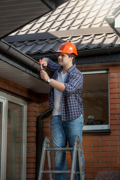 Foto trabajador de la construcción sonriente en la escalera bajo el techo de la casa