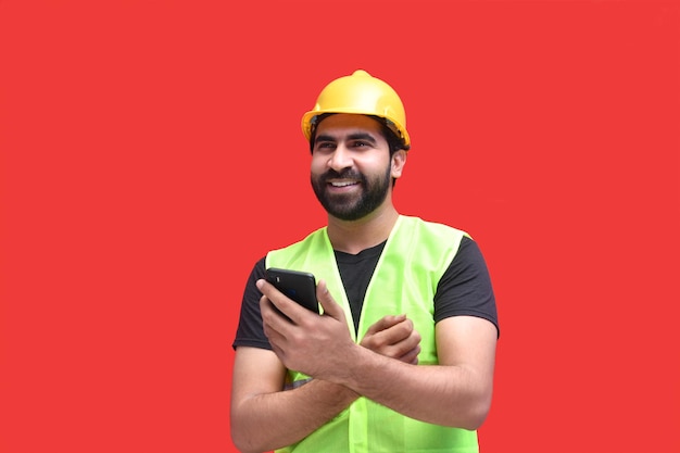 Trabajador de la construcción sosteniendo el teléfono posando sobre fondo rojo modelo paquistaní indio