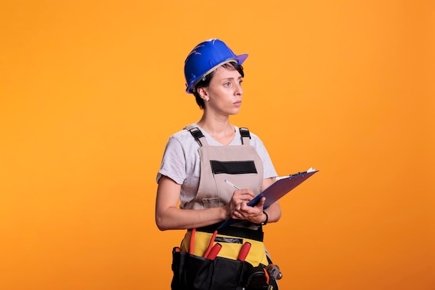 Trabajador de la construcción tomando notas y medidas para trabajar en el proyecto de renovación, sosteniendo papeles del portapapeles en el estudio. Joven ingeniero supervisor analizando información sobre archivos, habilidades industriales.
