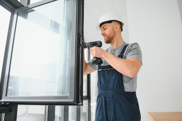 Trabajador de la construcción usando un taladro mientras instala una ventana en el interior