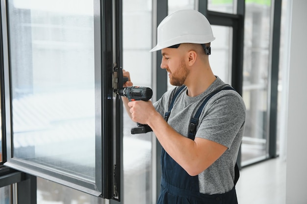 Trabajador de la construcción usando un taladro mientras instala una ventana en el interior