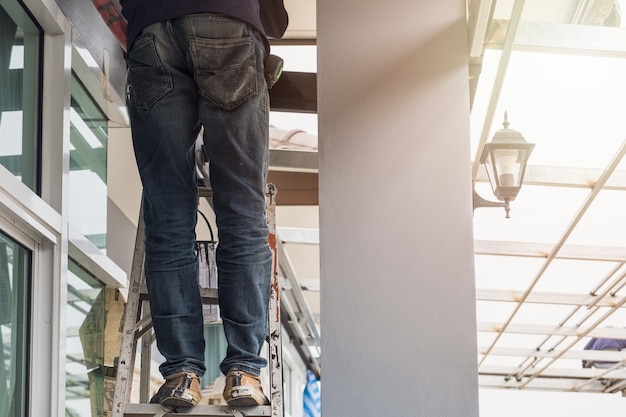 Foto trabajador de la construcción usar pantalón de jean de pie sobre escaleras de aluminio