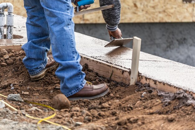 Trabajador de la construcción utilizando paleta de madera sobre cemento húmedo formando afrontamiento alrededor de la nueva piscina