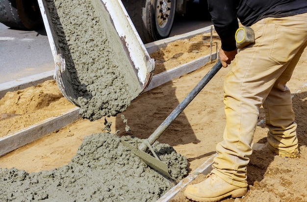 Foto trabajador de la construcción vierte cemento para acera en obras de hormigón con camión mezclador con carretilla