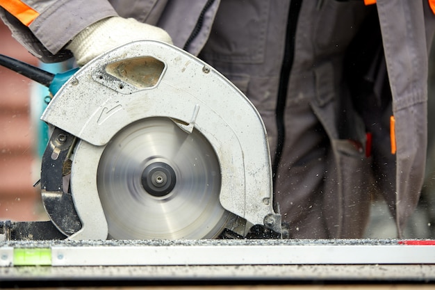 Un trabajador contratista de la construcción que utiliza una sierra circular manual de tornillo sin fin para cortar tablas y plástico. Construcción, taller propio, contratación de un contrato de trabajo de corte de madera.