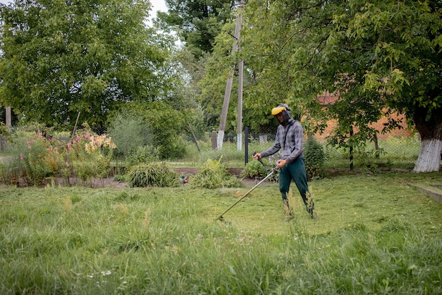 Trabajador con una cortadora de gas en sus manos, cortando césped en frente de la casa. Trimmer en manos de un hombre. Jardinero cortando el césped. Estilo de vida.