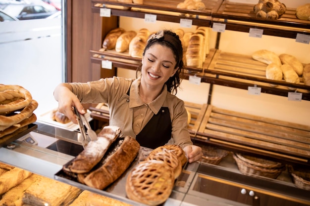 Trabajador de delicatessen en uniforme trabajando en el departamento de panadería del supermercado vendiendo pasteles a los clientes
