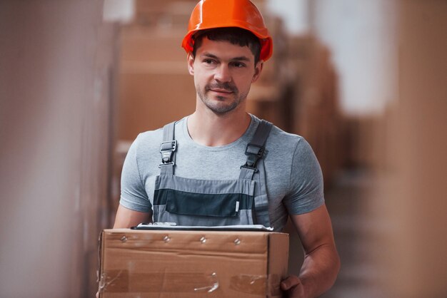 Foto trabajador en duro de color naranja está almacenado con caja en manos.