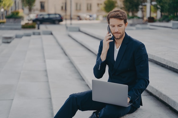 El trabajador ejecutivo del hombre habla por teléfono celular con un socio comercial utiliza una computadora portátil moderna