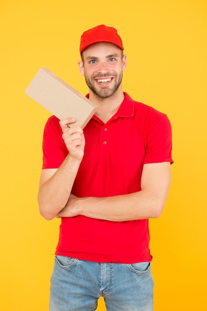 Trabajador de entrega de cartero. Fondo amarillo del casquillo rojo del hombre. Entrega de compra. Entregando felicidad y necesidades. Agente de mensajería súper rápido. Entrega de servicios. Carrera de vendedor. Mensajería y entrega.