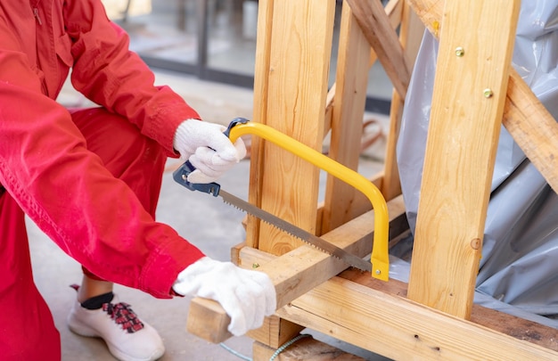 Un trabajador está aserrando madera para ensamblar una caja para mover una máquina industrial Una mujer de mecánico rojo