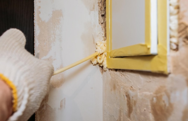 El trabajador está llenando espuma en aerosol cerca del panel eléctrico Reparación de mantenimiento trabajos de renovación en el piso Restauración interior