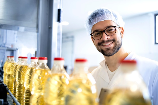 Trabajador de una fábrica de alimentos parado junto a la máquina de producción y verificando la calidad de la producción de aceite vegetal