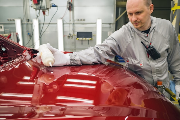 Trabajador de una fábrica de automóviles pule la superficie pintada